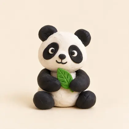 A clay panda holding a green leaf, made by a child